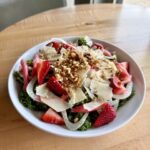 Strawberry rhubarb salad with kale, shaved fennel, fresh strawberries, rhubarb, parmesan, candied pecans, and champagne vinaigrette, served as a vegetarian and gluten-free spring dish