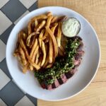 Steak frites with grilled hanger steak, chimichurri, crispy fries, and garlic aioli.